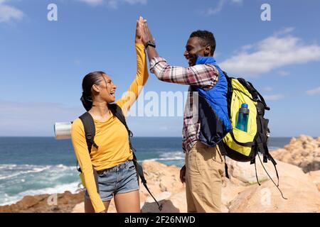 Fit afrcan american couple wearing backpacks high fiving hiking on the coast Stock Photo