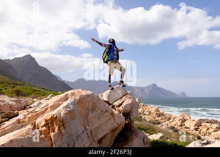 Fit afrcan american man wearing backpack hiking spreading arms on the coast Stock Photo