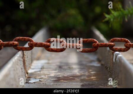 A selective focus shot of a massive rusty iron chain over a rural irrigation canal Stock Photo
