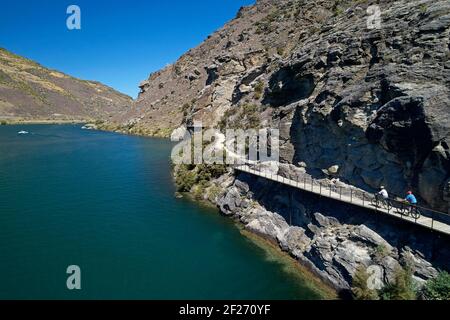 Cyclists on cantilever bridge on Lake Dunstan Cycle Trail, and Lake Dunstan, near Cromwell, Central Otago, South Island, New Zealand Stock Photo
