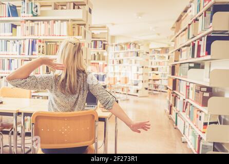Learning for exams: tired female student in the university library, pile of books Stock Photo