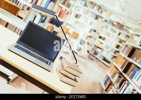 Studying in the university: Laptop on a wooden desk, pile of books and books in the blurry background Stock Photo