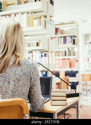 Student in pile of books in library Stock Photo - Alamy