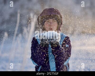 Portrait of girl blowing snowflakes to camera in winter, focus on snow Stock Photo