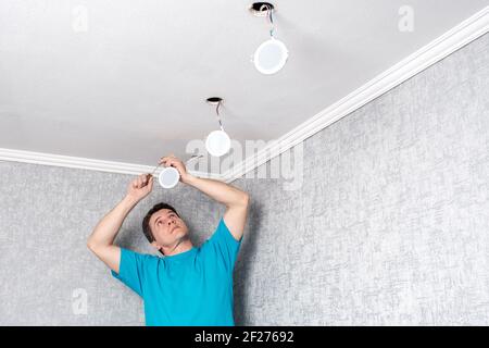 electrician installing modern LED ceiling spotlights. Stock Photo