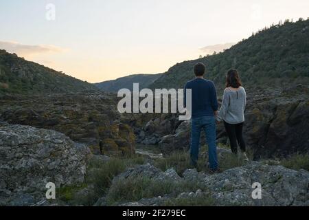 Couple looking holding hands at Pulo do Lobo waterfall with river guadiana and rock details at sunset in Mertola Alentejo, Portu Stock Photo
