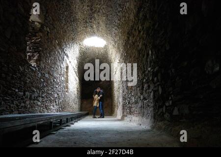 Romantic couple kissing on a dark ruin antique temple arab muslim church tunnel room with a hole where light comes through Stock Photo