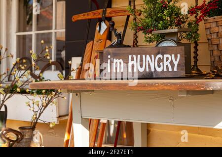 A porch decor consisting of an old wooden table with a rustic vintage kitchen scale, a straw basket, some decorative redwood plants and a wooden sign Stock Photo