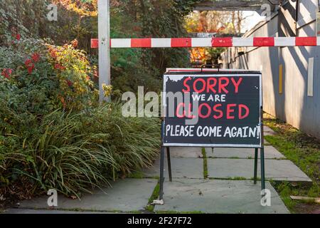 A large blackboard sign post in front of a shop says: " Sorry We are closed, please come again." There is a road block ahead. A concept image for buss Stock Photo