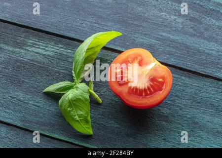 A closeup of a fresh organic heirloom tomato with vibrant green basil leaves, on a dark wooden background Stock Photo