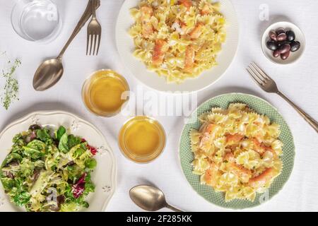 Two plates of salmon pasta. Farfalle with smoked salmon and cream sauce, shot from the top with wine and salad leaves Stock Photo