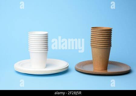 Stack of white and brown paper cups and round plates on a blue background Stock Photo