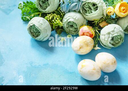 Happy Easter background. Spring flowers and Easter eggs on a concrete blue background. Stock Photo