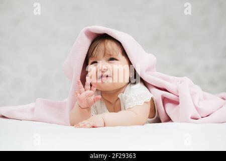 Crying six months old baby girl lying on blanket at home Stock Photo