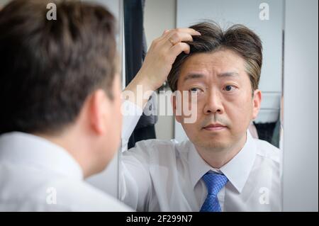 Asian middle-aged man looking in the mirror and touching his hair Stock Photo