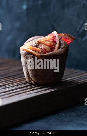 Brownie muffin with blood orange slices on ribbed oak cutboard on dark plaster background front view Stock Photo
