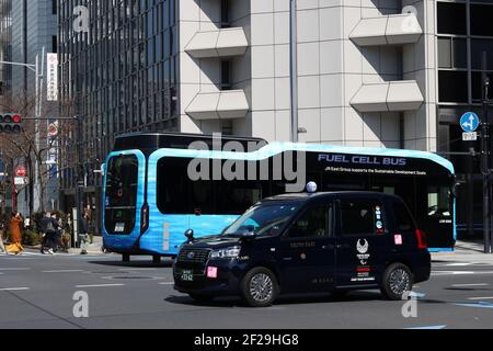 A taxi and a fuel cell bus, a JR East-operated SORA Fuel Cell, on a road in central Tokyo near Tokyo Station. The taxi is a Toyota JPN taxi. (3/2021) Stock Photo