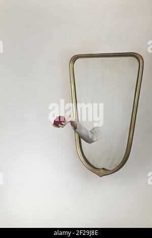 surreal gesture of a hand coming out of the mirror to give a rose Stock Photo