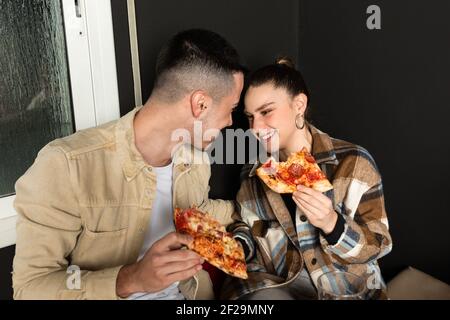 a young caucasian couple gazes at each other romantically while eating pizza Stock Photo