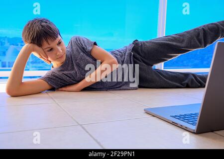 Child watching online video on laptop computer and doing sport fitness exercises on balcony at home Stock Photo
