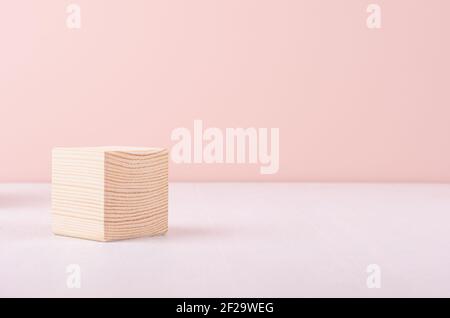 Beige natural wood podium of cube shape on white wood table and pastel pink wall. Showcase for cosmetic products, packings. Stock Photo