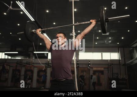 Low angle shot of a strong muscular cross fit athlete lifting heavy barbell overhead Stock Photo