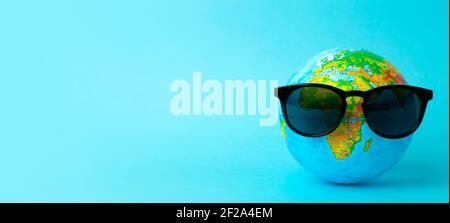 Tourism, ecology, vacation and globalism concept. Globe in sunglasses on a blue banner background. Minimal creative. High quality photo Stock Photo