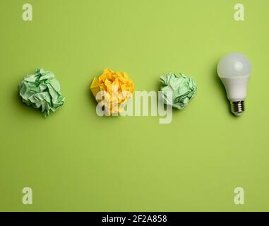 crumpled colored balls of paper and glass white lamp on green background, top view Stock Photo
