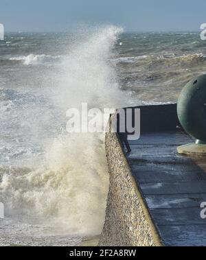 Brighton UK 11th March 2021 - A photographer captures the waves crashing onto Brighton seafront as stormy weather batters the South Coast today : Credit Simon Dack / Alamy Live News Stock Photo