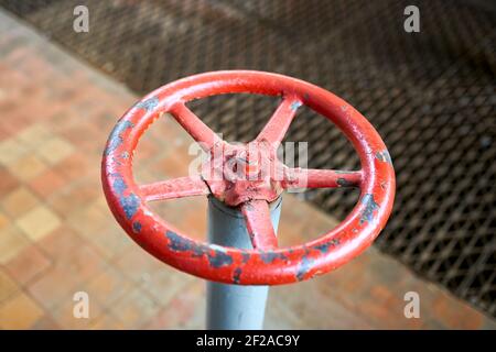 Old rusty painted red valve wheel with swellings and peeling selective focus with extension device over out of focus background tiled floor and Stock Photo