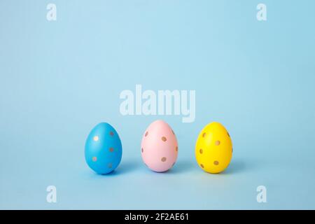 Three colored decorated eggs on a blue background. Easter greeting card in minimalist style concept.Copy space Stock Photo