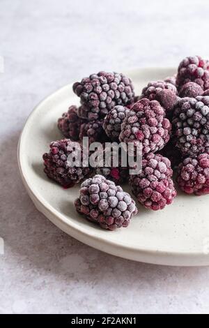 Close up of frozen blackberries on a pale ceramic plate. Stock Photo