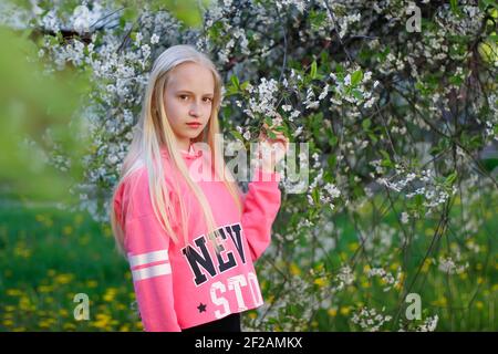 Pretty teen girl are posing in garden near blossom tree with white flowers. Spring time Stock Photo