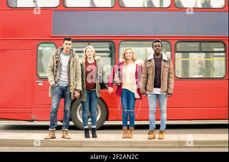 Group of friends crossing the road with traditional red bus behind - Autumn or winter concept of social life with young people hanging out together Stock Photo