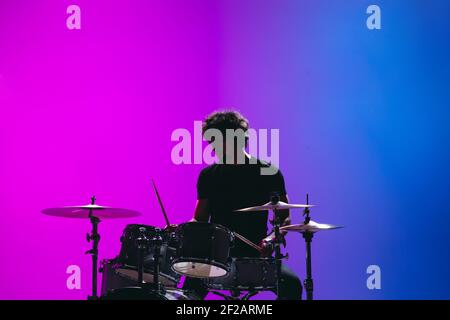 Silhouette of young man drummer playing isolated on blue-pink background in neon Stock Photo