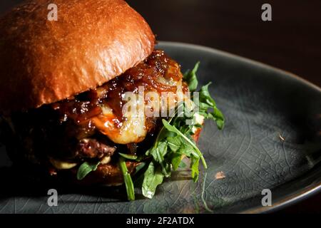 Juicy beef burger with caramelized onion, cheese and rucola on homemade bun. Stock Photo