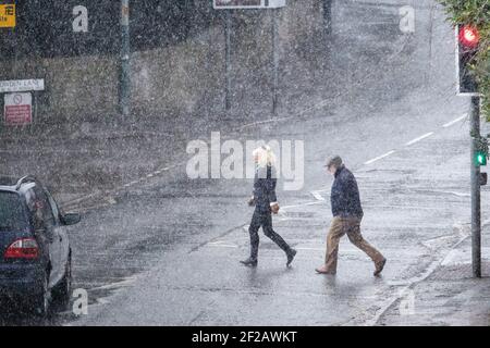 Chippenham, Wiltshire, UK, 11th March, 2021. Pedestrians are pictured braving heavy rain in Chippenham as heavy rain showers make their way across Southern England. Credit: Lynchpics/Alamy Live News Stock Photo
