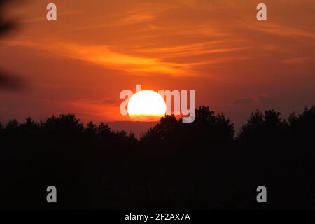 Sunset - sky on fire, sun dial, sky on fire, red sky, silhouette, trees, summer sunset - sun is setting behind the trees Stock Photo