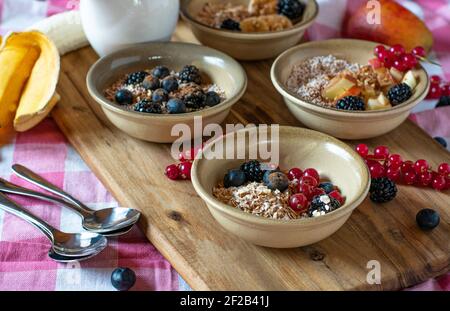 Bowls with a variation of different breakfast muesli such as granola, cereal, oatmeal, amaranth pops and millet served with fruits on wooden table Stock Photo