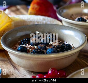 Delicious blueberry, blackberry oatmeal with roasted almonds and cinnamon served in rustic stoneware bowl on kitchen table Stock Photo