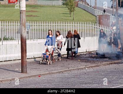 BELFAST, UNITED KINGDOM - JUNE 1972. School Children passing infront of British Army Soldiers and Burning Hijacked vehicle, Ballymurphy, West Belfast during The Troubles, Northern Ireland, 1970s Stock Photo