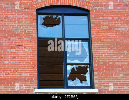 Close-up of a window, in a brick wall, in which all but one pane of glass has been broken. Stock Photo