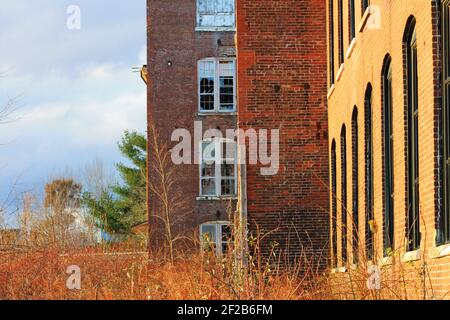 An old, abandoned, brick building that is falling into ruin, with broken windows and overgrown yard. Stock Photo