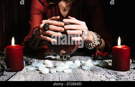 Fortuneteller's hands on a glass orb. Prediction of the future. Mystic interior. Occult symbols, runes stones, candles Stock Photo