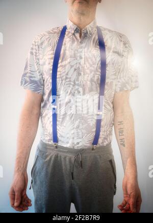 Mid adult man with arm tattoo standing in sunlight wearing suspenders, summer shirt and sweatpants. People, fashion, lifestyle concept Stock Photo