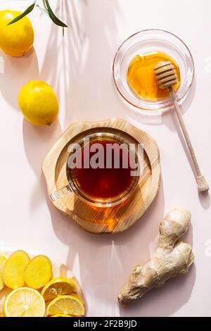 A cup of ginger tea, honey, lemon and ginger root, flat lay on a pink background. The modern wellness concept. Vegan, healthy food, boosting immunity. Stock Photo