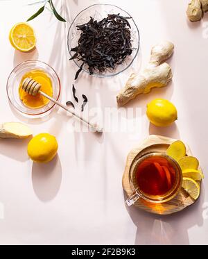 A cup of ginger tea, honey, lemon and ginger root, flat lay on a pink background. The modern wellness concept. Vegan, healthy food, boosting immunity. Stock Photo