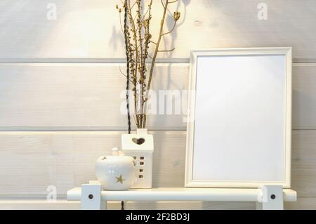 Wooden white wall in a scandinavian house, mockup of a white photo frame on a shelf, dry flowers. Stock Photo