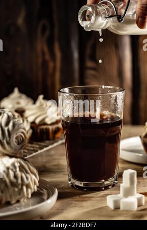 Pouring milk into a glass of hot coffe. Stock Photo