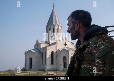 SHUSHI, NAGORNO KARABAKH - NOVEMBER 03: An ethnic Armenian wearing a military fatigue stands in front of the Armenian Apostolic Holy Savior Cathedral commonly referred to as Ghazanchetsots during a military conflict between Armenian and Azerbaijani forces over the disputed Nagorno-Karabakh region known also as the Artsakh Republic in the town of Shushi or Shusha in the self-proclaimed Republic of Artsakh or Nagorno-Karabakh, de jure part of the Republic of Azerbaijan on November 03 2020. The fighting between Armenia and Azerbaijan over Nagorno-Karabakh known also as the Artsakh Republic re-eru Stock Photo
